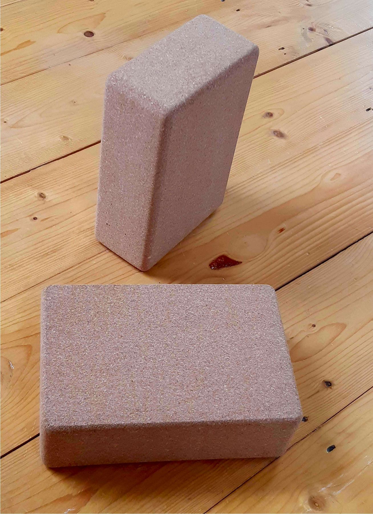Pair of cork yoga bricks stacked on a wooden floor, representing Yogasya's Yoga Props category